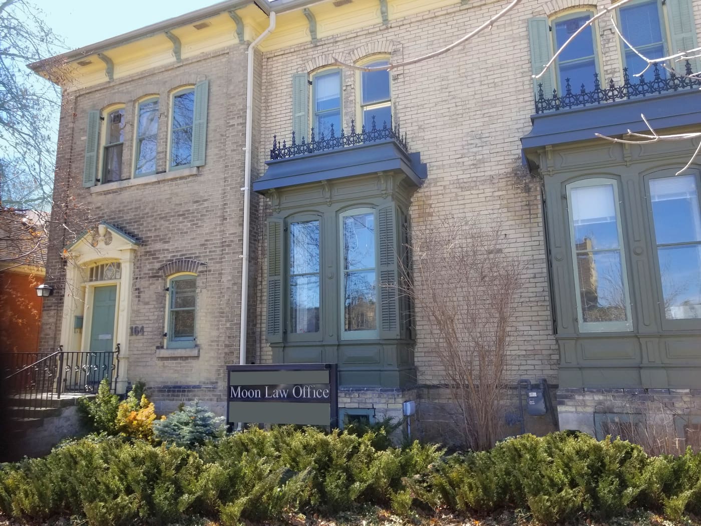 The Moon Law Office at 164 Norfolk St: a two-storey yellow brick building with green bay windows and the Moon Law Office sign behind a low hedge.